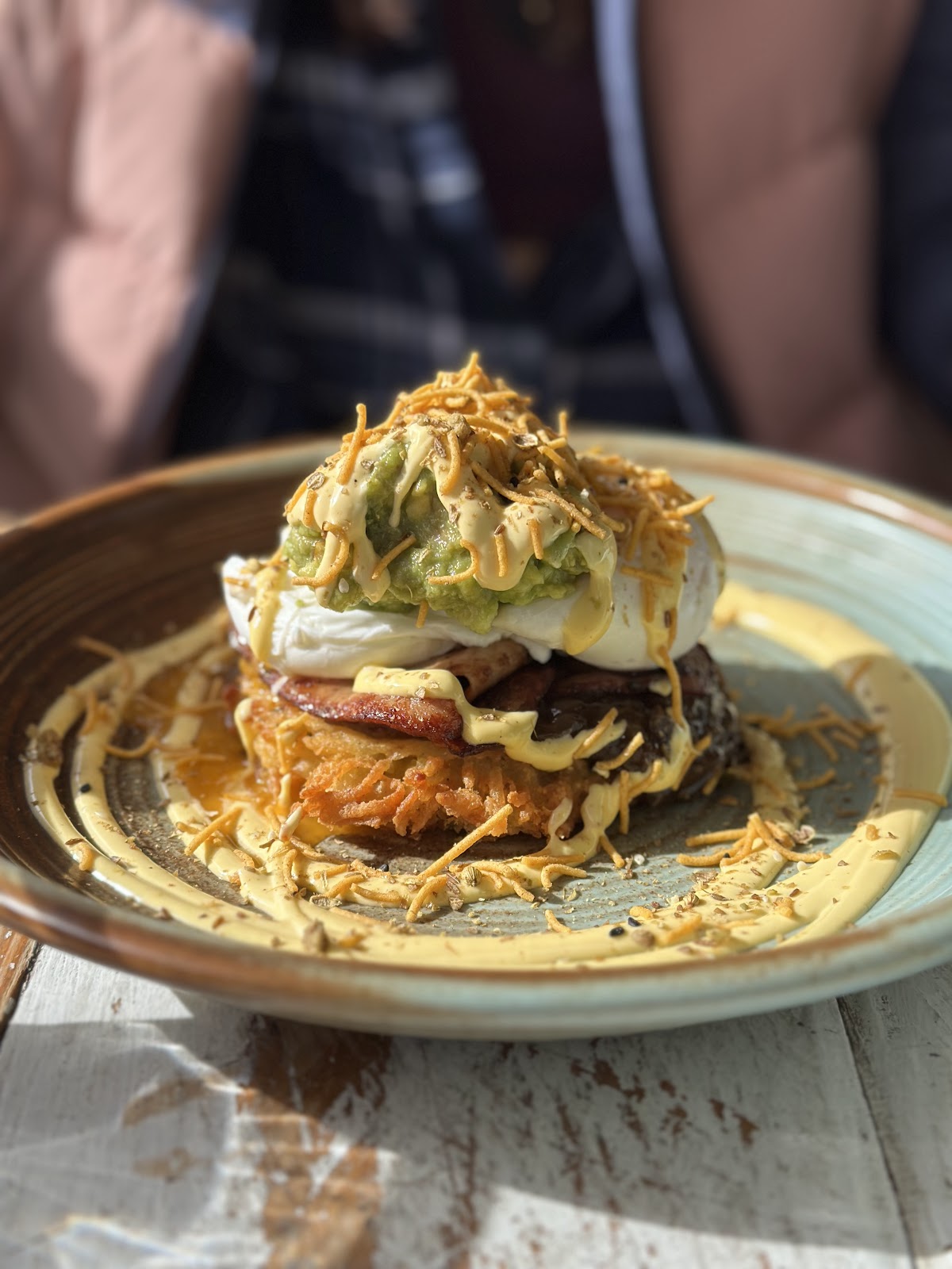 Poached egg, bacon and smashed avocado stacked on a crispy potato rosti