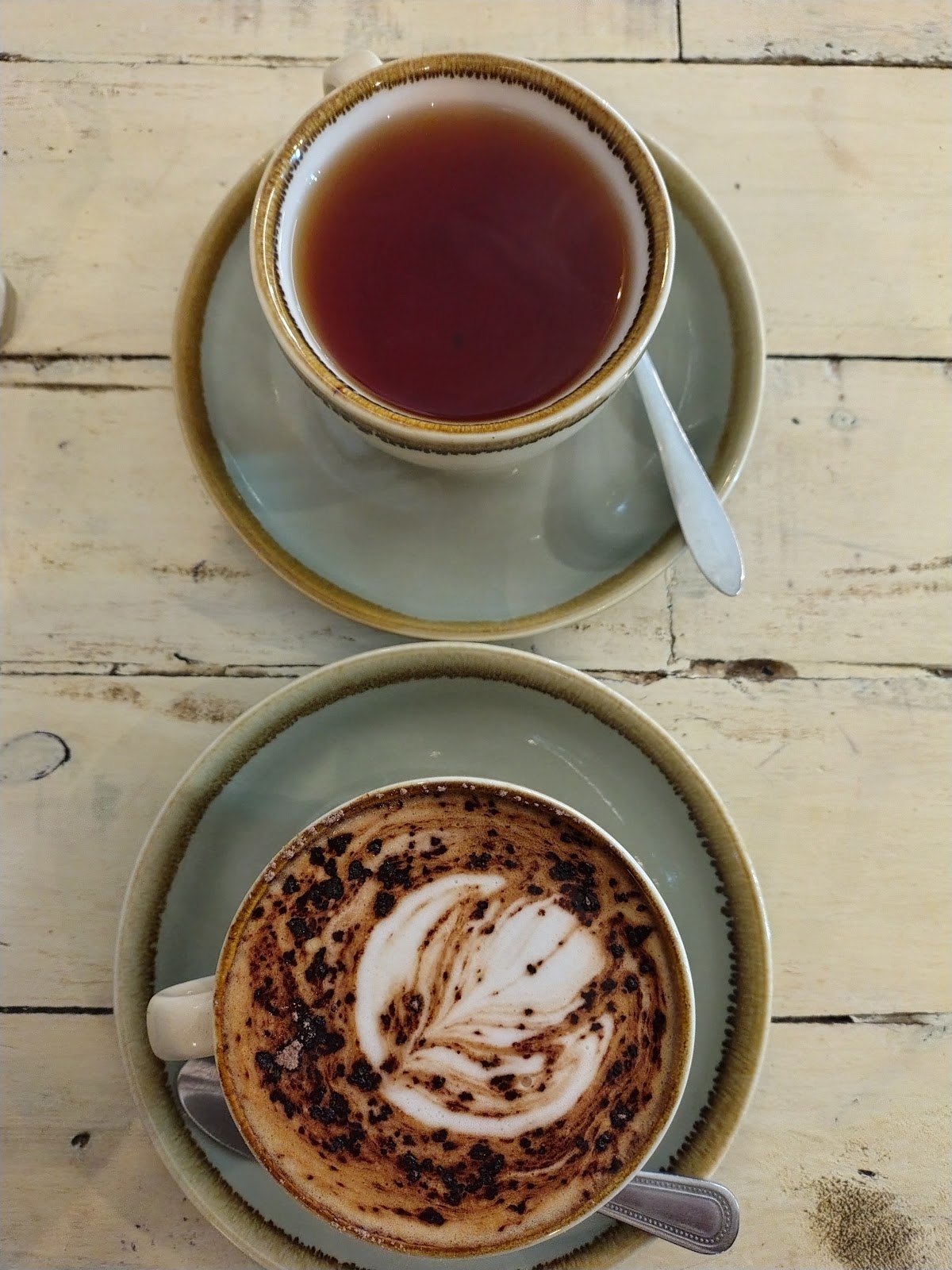 A pot of tea and a cappuccino on a whitewashed timber table