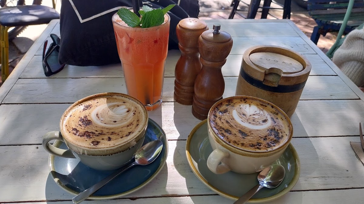 Two cappuccinos and a watermelon and mint juice on an outdoor table on Dean Street
